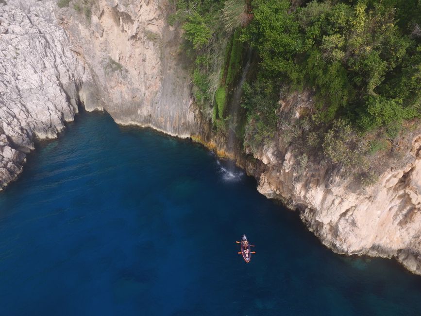 Stunning aerial shot of a canoe navigating a turquoise cove near a rocky cliff in Muğla, Türkiye.