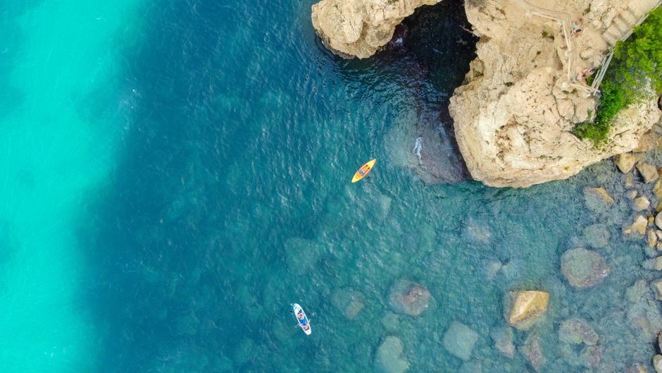 A stunning aerial view showcasing kayaks near rocky cliffs on the Spanish coast, with clear blue waters.