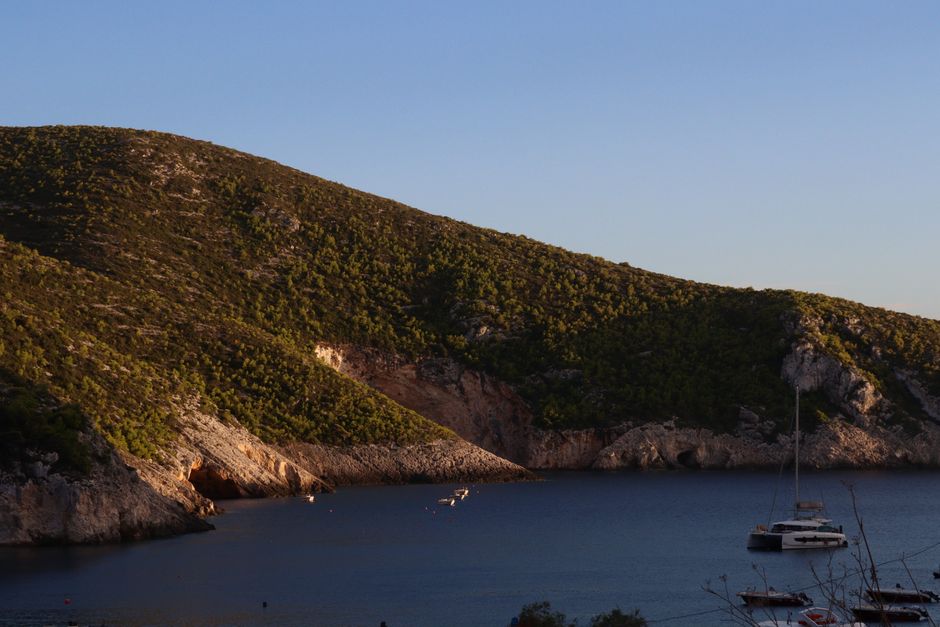 A tranquil view of a Mediterranean cove with sailboats at sunset.