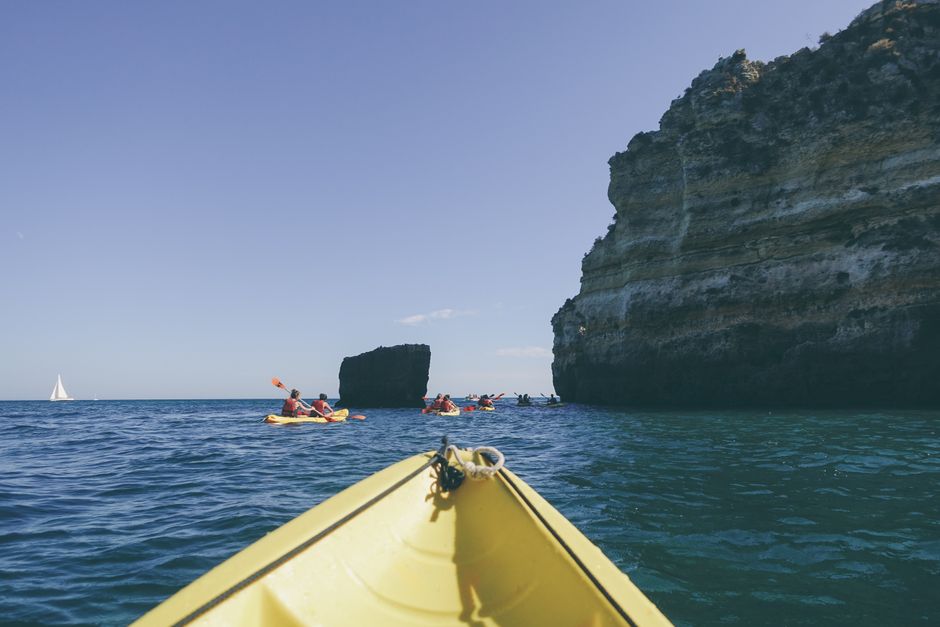 Group of kayakers paddling near rocky cliffs and open sea under clear sky.